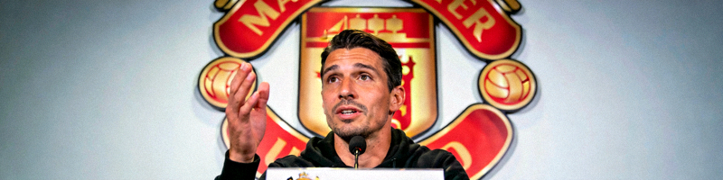 足球运动员在新闻发布会上回答记者提问，背景是球队队徽